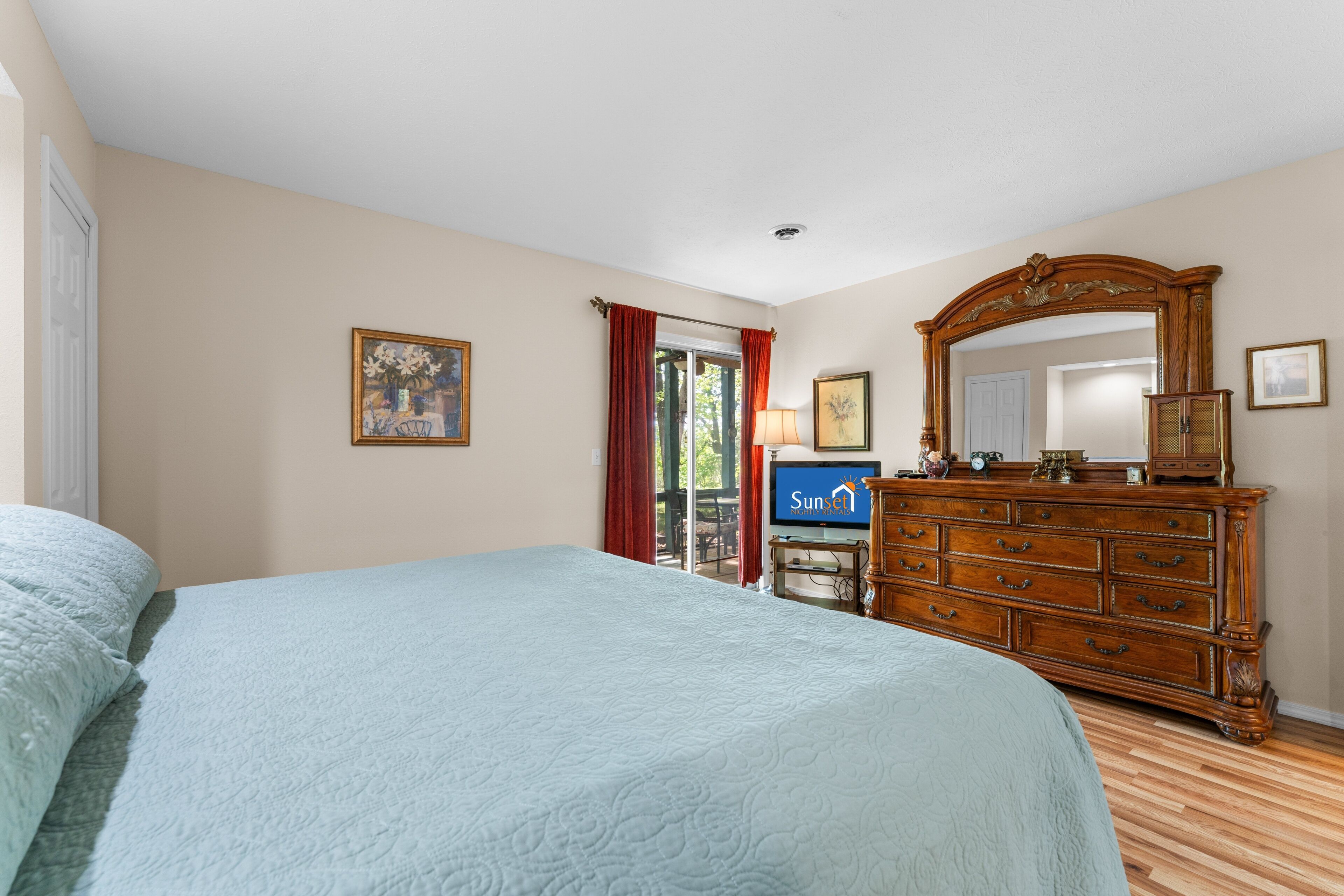 Une chambre à coucher avec un grand lit, une commode, un téléviseur et une porte donnant sur un balcon.