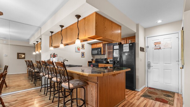 Una cocina con armarios de madera, una isla central, taburetes de bar, un refrigerador y un microondas.