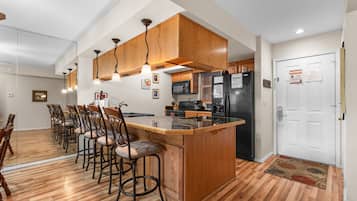 Una cocina con armarios de madera, una isla central, taburetes de bar, un refrigerador y un microondas.