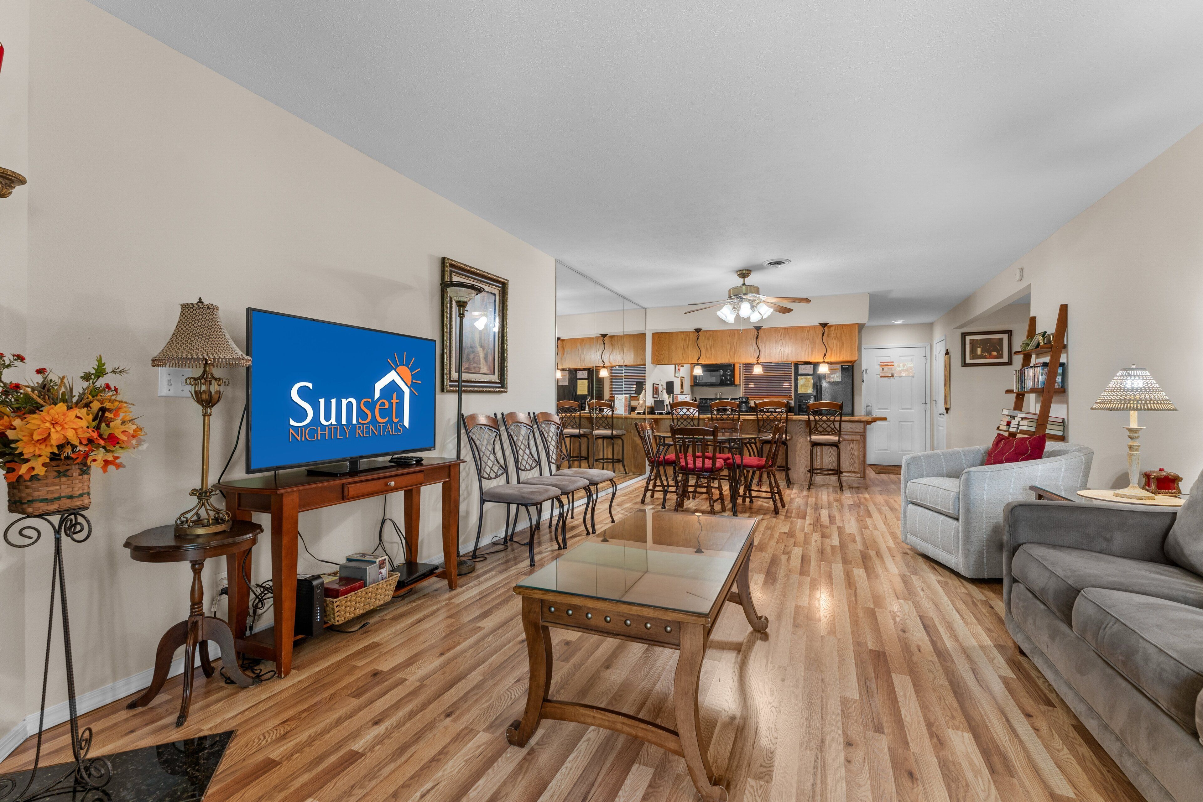 A living room with a television, dining area, kitchen, and a ceiling fan.
