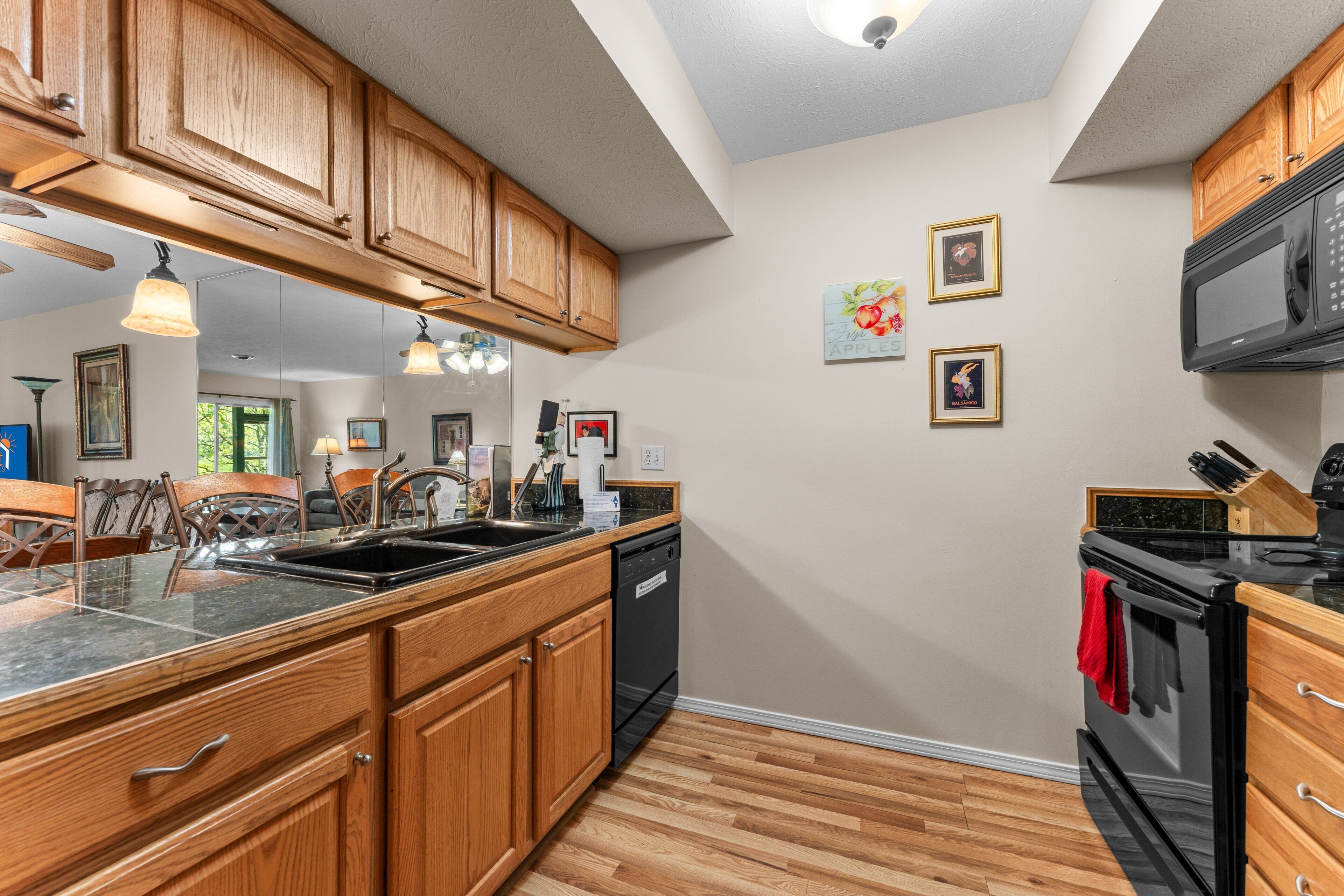 A kitchen with wooden cabinets, a black dishwasher, a microwave, and a stove. There are framed pictures on the wall.