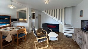 Un espacio habitable moderno con comedor, sofá, televisor y escalera.