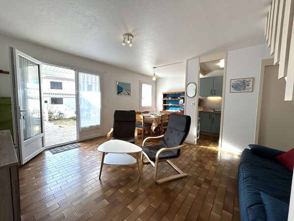 A spacious living area with a wooden floor, a dining table, a sofa, and a kitchen area visible through an open door.