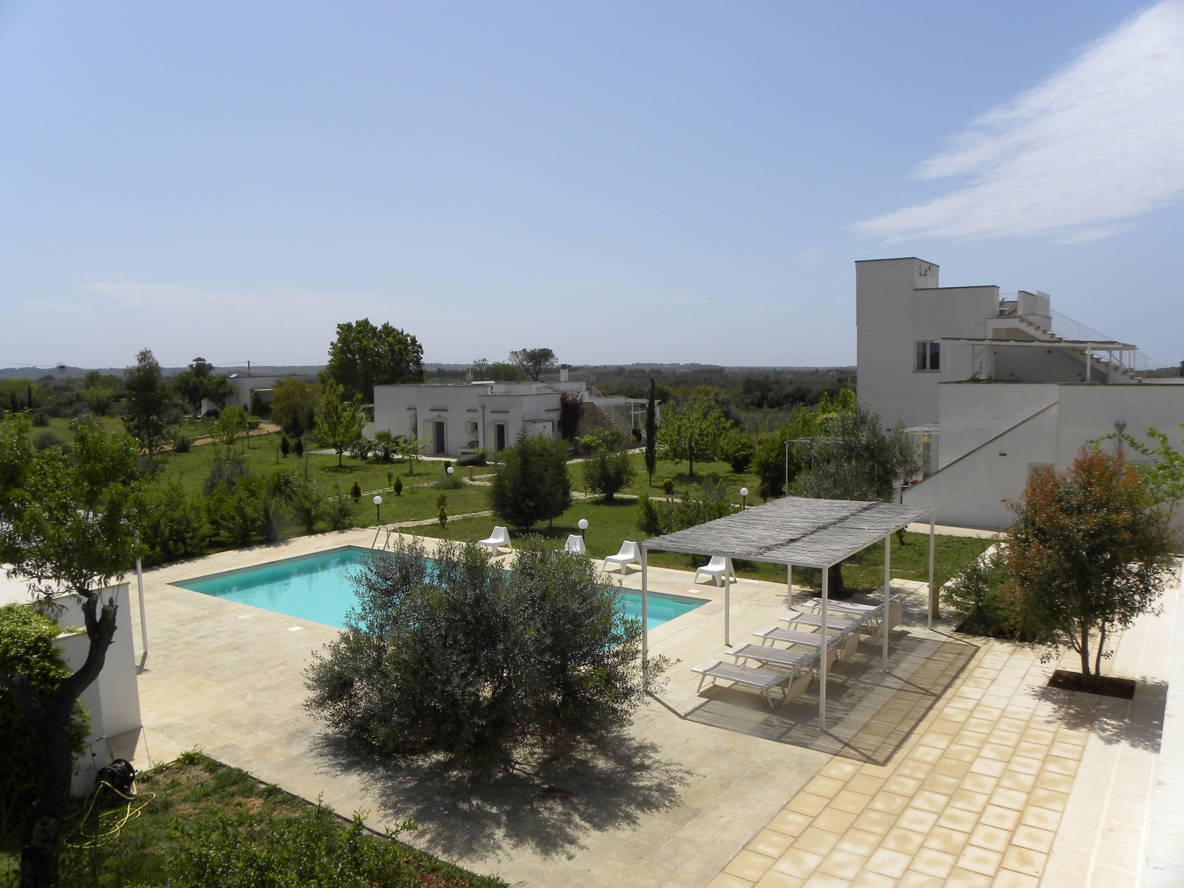 Un área de piscina moderna al aire libre con vistas despejadas del paisaje circundante, que incluye un edificio grande y abundante vegetación.