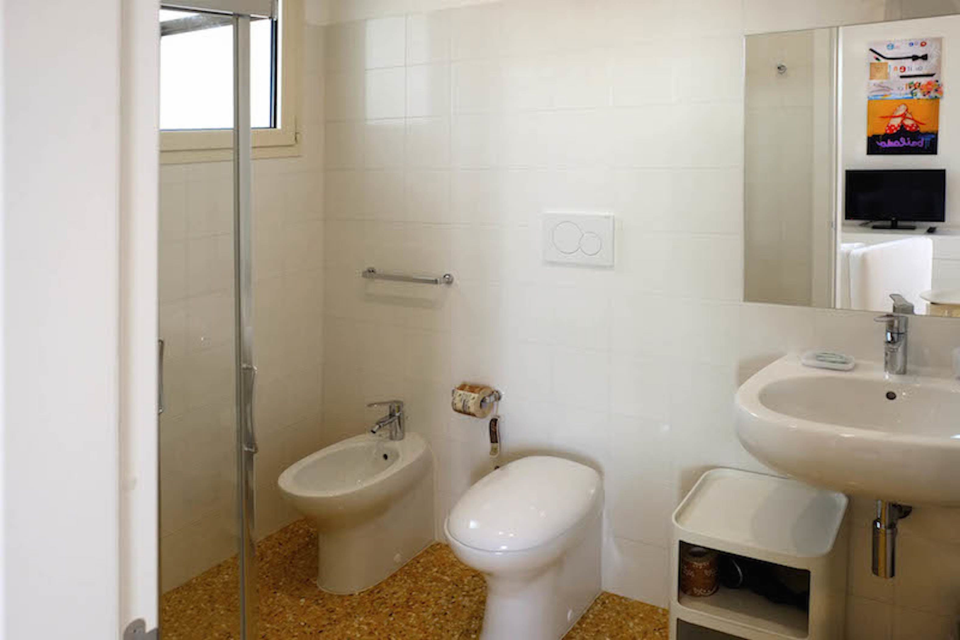 A bathroom with a shower, bidet, toilet, sink, and a small shelf.