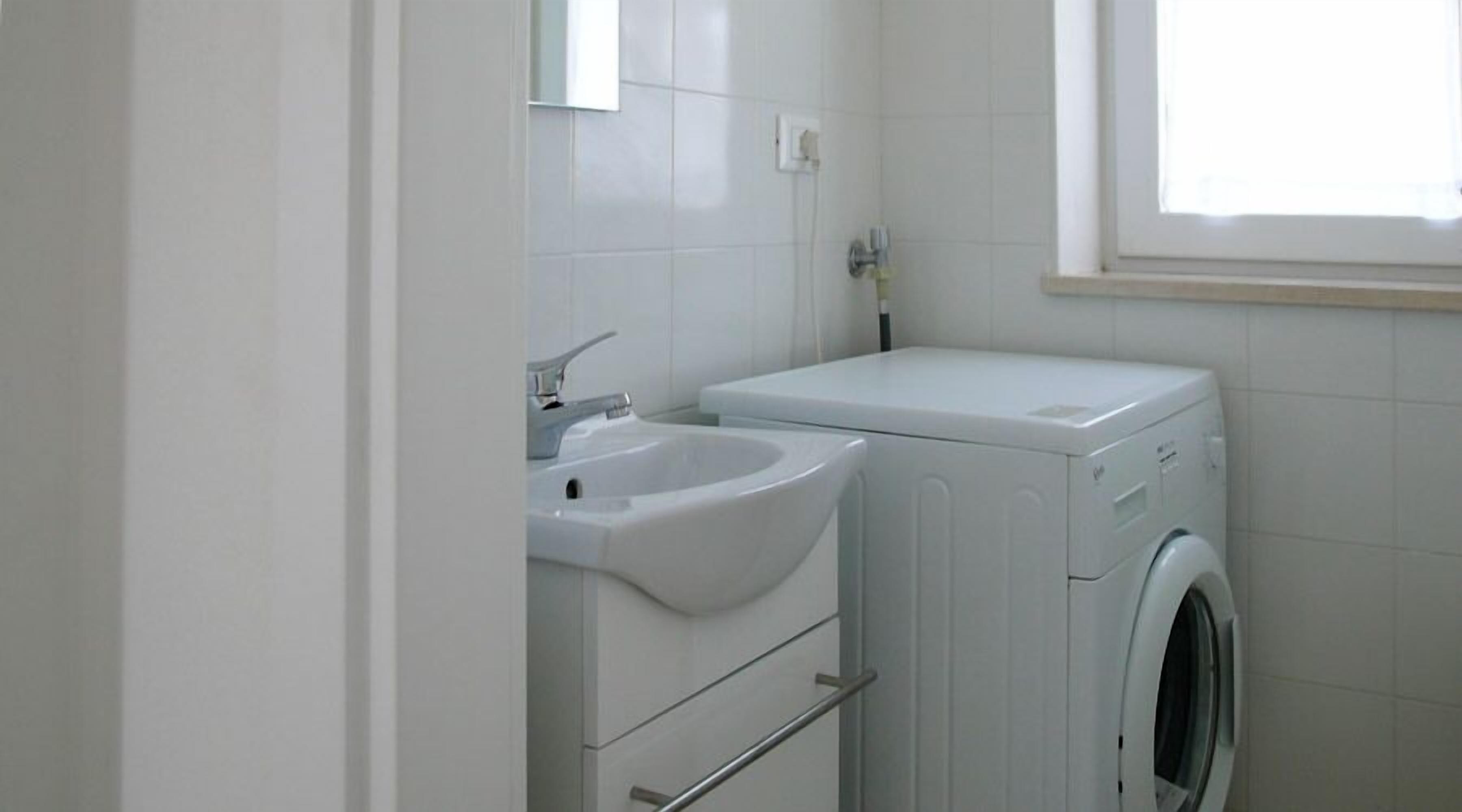 Un baño pequeño y limpio con lavamanos, espejo y lavadora.