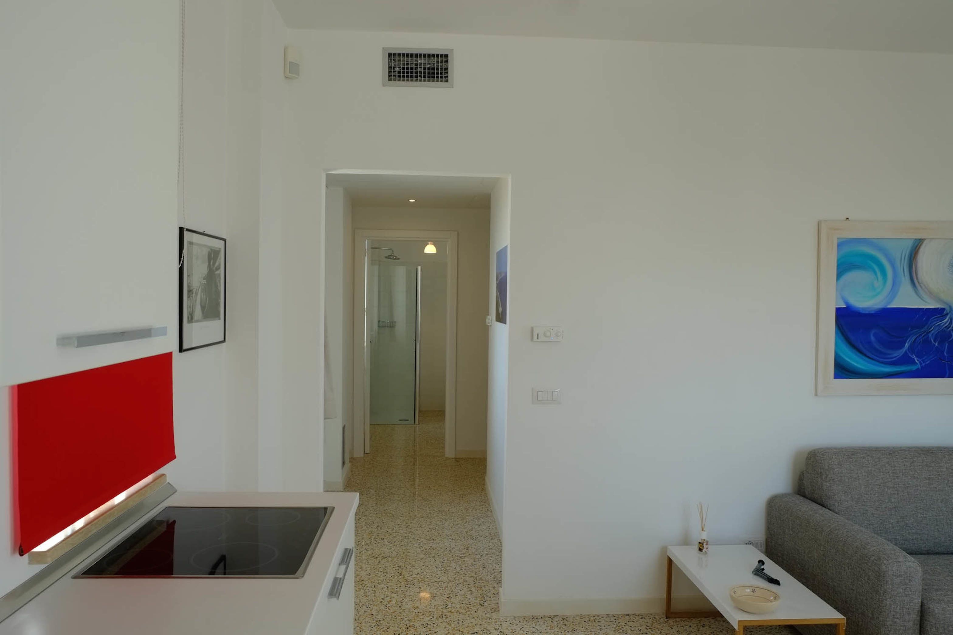 A modern room with a kitchen area, a hallway leading to a bathroom, and a living area with a sofa and a small table.