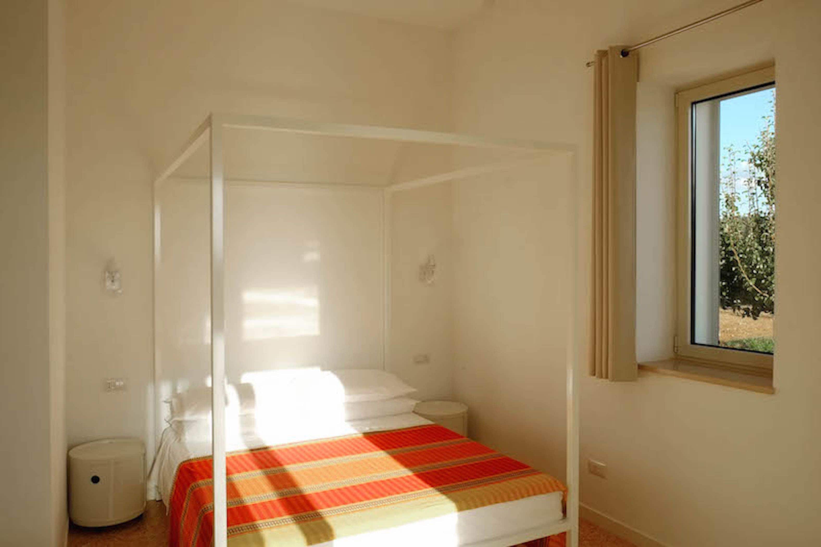Ein Bett mit Baldachin in einem Zimmer mit Fenster und einem kleinen Mülleimer.