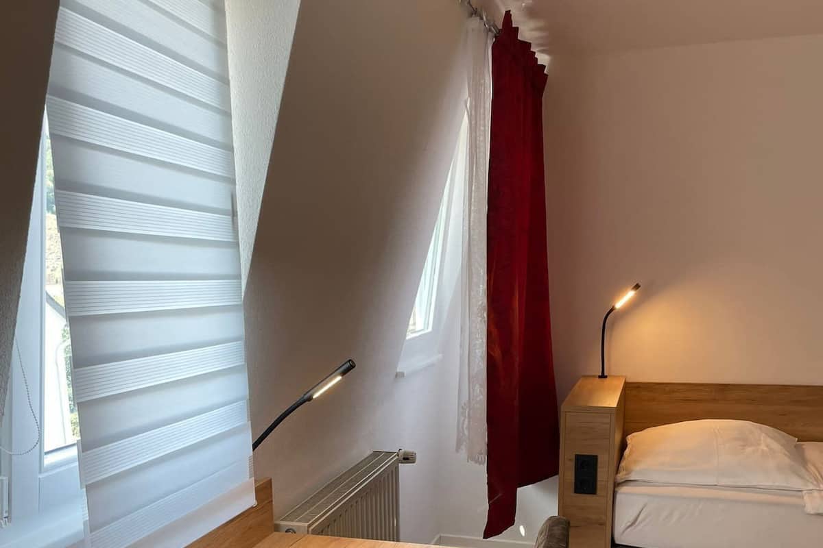Een slaapkamer met een bed, een bureau, een stoel, een radiator en een raam met jaloezieën.