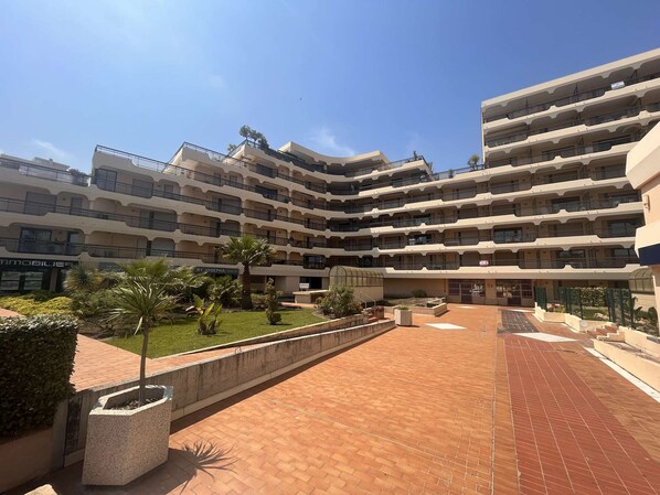 Hotel de vários andares com um pátio central, apresentando um caminho de tijolos e áreas ajardinadas com palmeiras.