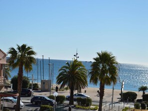 Uma rua costeira com palmeiras, carros estacionados e vista clara para o mar.
