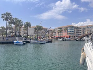 A marina with boats docked, palm trees, and a building with balconies. - Seaside studio cabin, 4 pers, terrace, quiet residence (Fréjus)