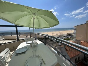 Varanda com mesa posta para refeições, com vista para a praia e o mar.