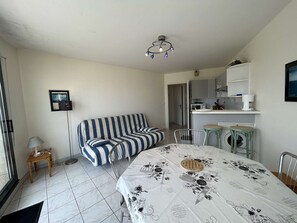Quarto compacto com cama, sofá listrado, mesa pequena, cadeira, máquina de lavar e cozinha compacta.