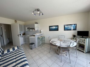 Um espaço compacto com cozinha compacta, área de jantar com mesa e cadeiras, sofá e televisão.