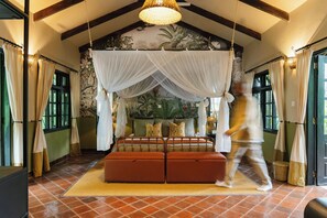 A room with a bed under a canopy, a large window, and a tropical mural on the wall.