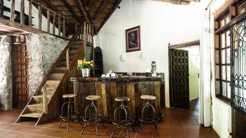 Un interno rustico con una scala in legno, pareti in pietra, un’area bar con sgabelli e un quadro appeso al muro.