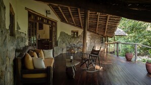 A rustic wooden deck with stone walls, a thatched roof, and a dining area with wooden furniture. - Rivertrees Country Inn (Arusha)