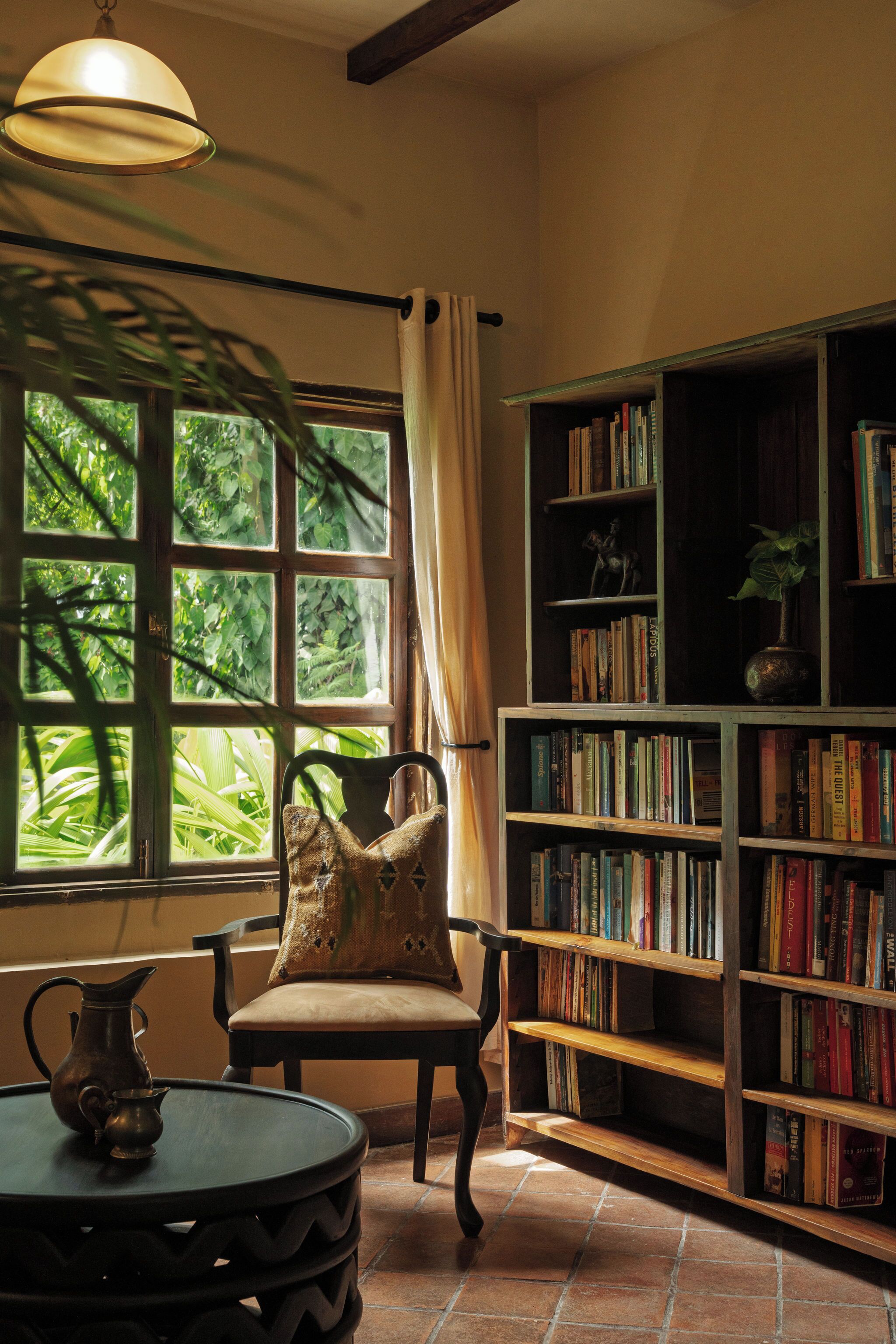 A cozy reading nook with a chair, a small table with a pitcher, and a bookshelf filled with books.