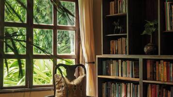 Un rincón acogedor para leer, con una silla, una mesita con una jarra y una estantería llena de libros.