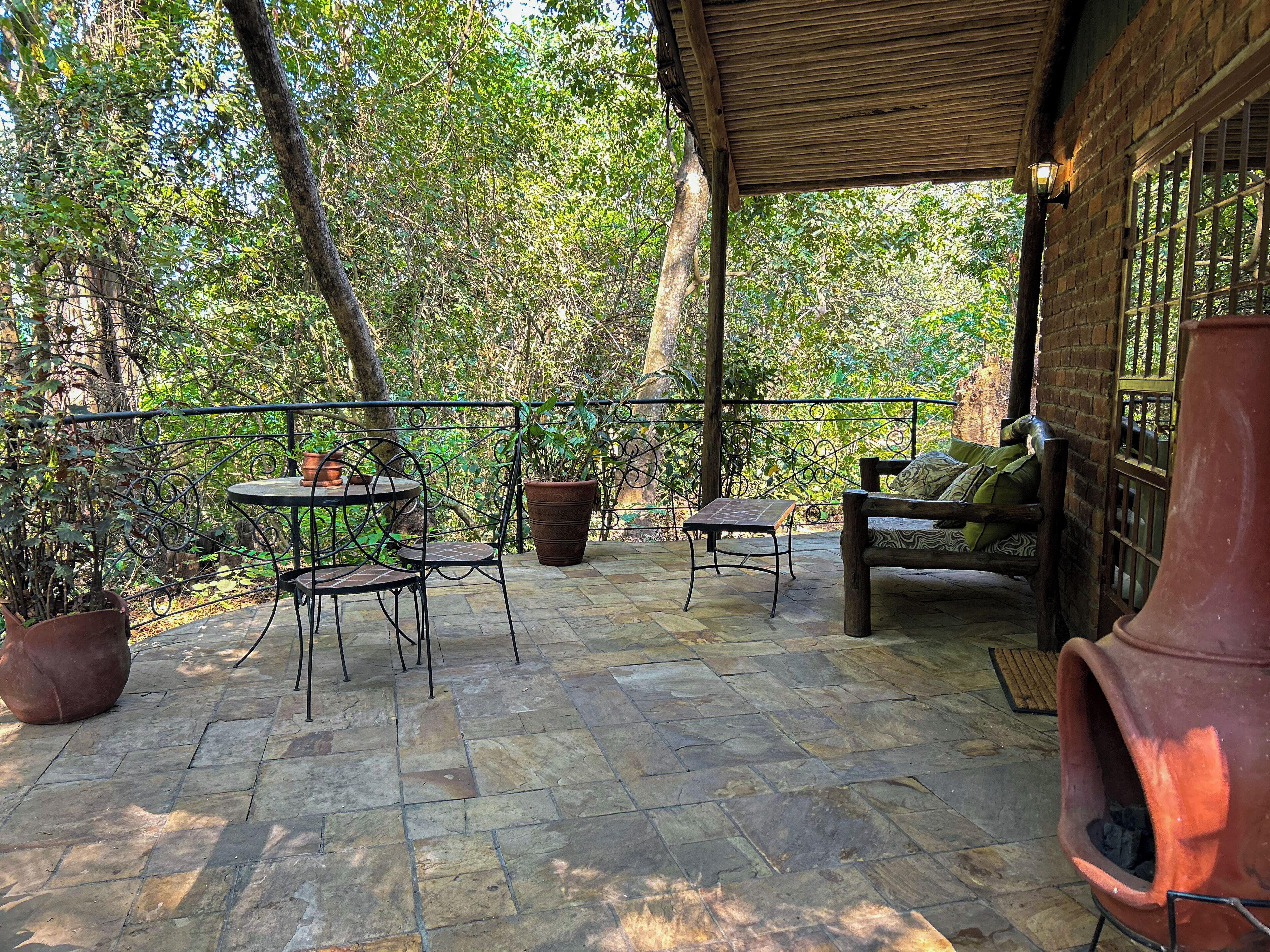 An outdoor patio with stone flooring, metal chairs, a table, a sofa, and potted plants.