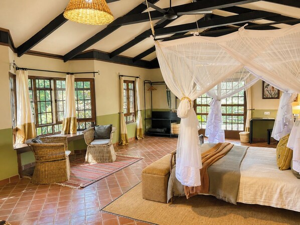 A room with a bed, two chairs, a sofa, a television, and a large window with curtains. - Rivertrees Country Inn (Arusha)