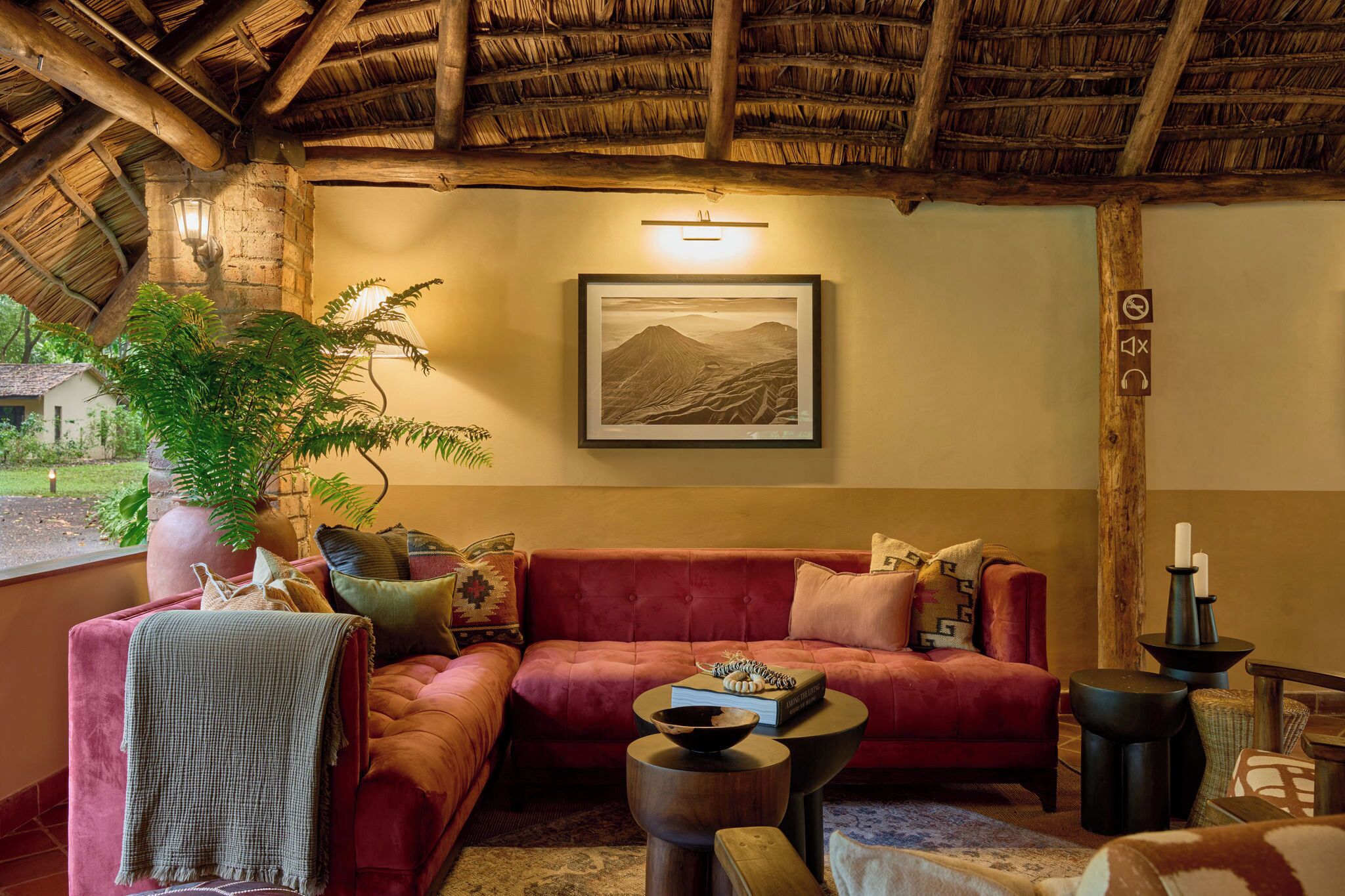 A cozy living area with a red sofa, a large potted plant, and a framed landscape painting on the wall.