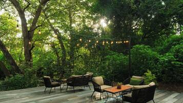 Un patio exterior con suelo de madera, muebles de mimbre e iluminación con guirnaldas.