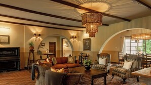 A cozy living room with a fireplace, comfortable seating, and a chandelier. - Rivertrees Country Inn (Arusha)