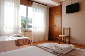 A bedroom with two beds, a wooden wardrobe, a chair, and a TV on the wall. - La Terraza de Picos (Cabrales)
