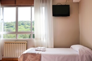 A bedroom with a bed, a TV mounted on the wall, a window with curtains, and a radiator. - La Terraza de Picos (Cabrales)