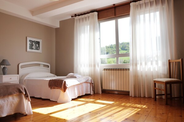 A bedroom with two beds, a radiator, a chair, and a window with curtains. - La Terraza de Picos (Cabrales)