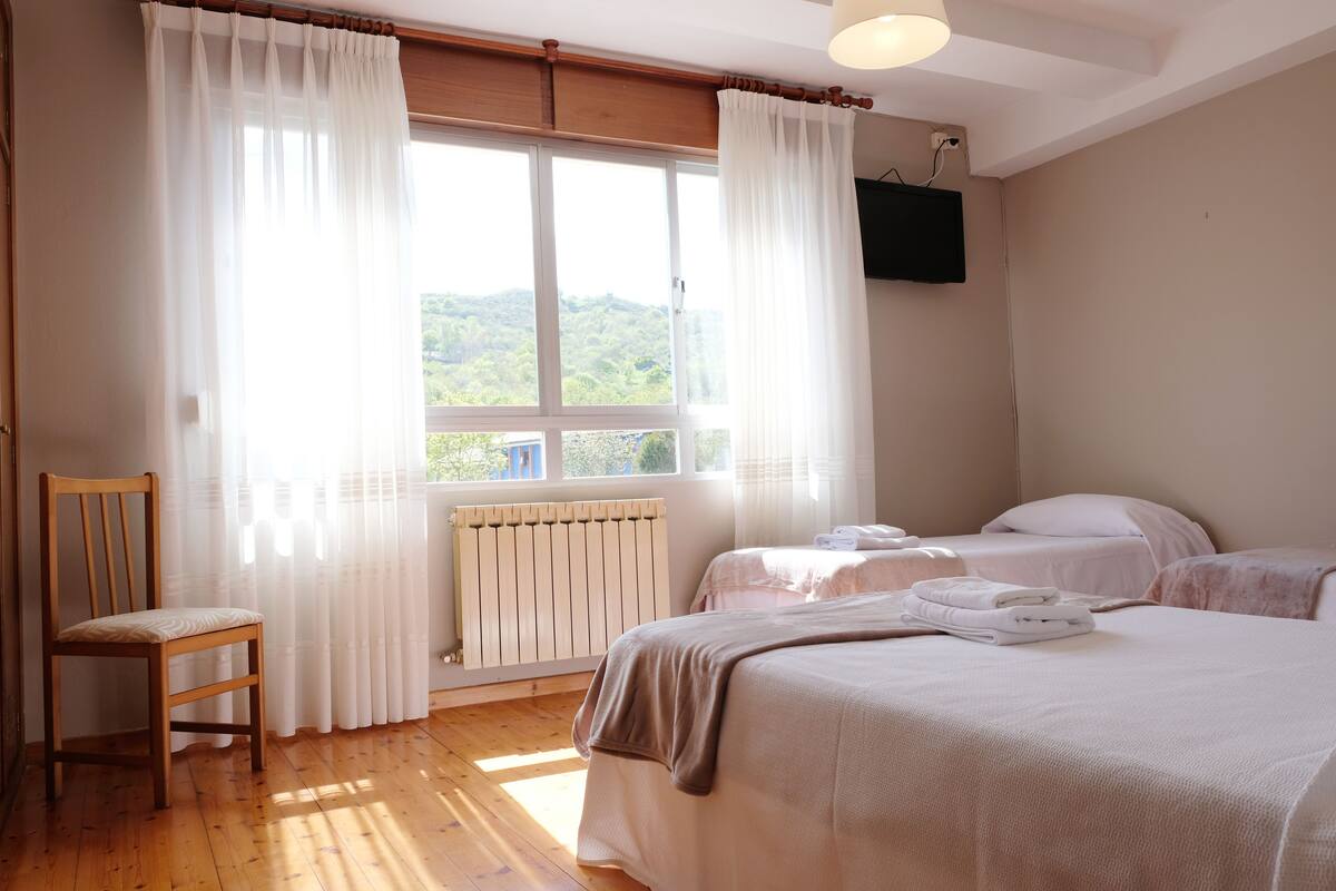 A bedroom with two beds, a chair, a radiator, and a window with curtains.