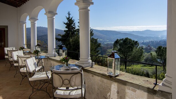 A covered outdoor seating area with white chairs and tables, overlooking a scenic landscape with mountains and trees. - Il Verreno (Ambra)