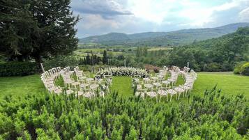 A circular arrangement of white chairs in a grassy outdoor area with a backdrop of hills and trees.