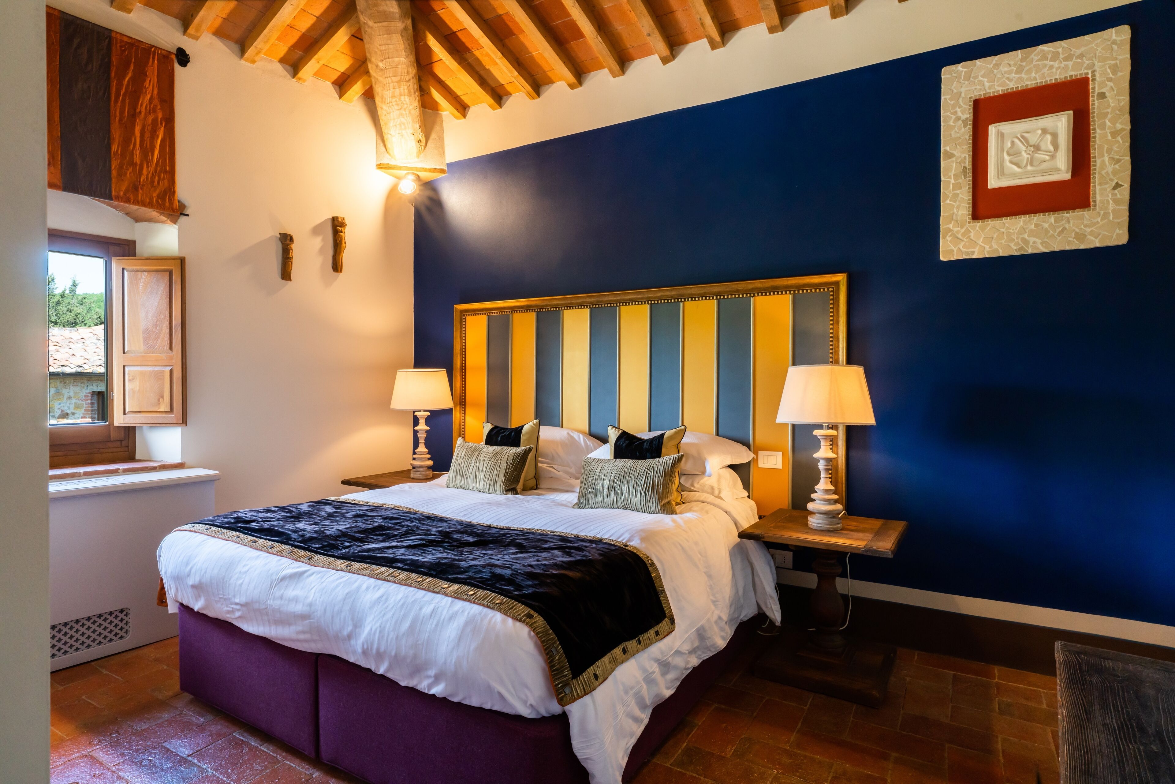 Un dormitorio con una cama grande, dos lámparas de noche, un cabecero de madera y un ventanal con vistas a la vegetación.