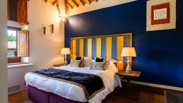A bedroom with a large bed, two bedside lamps, a wooden headboard, and a window with a view of greenery.
