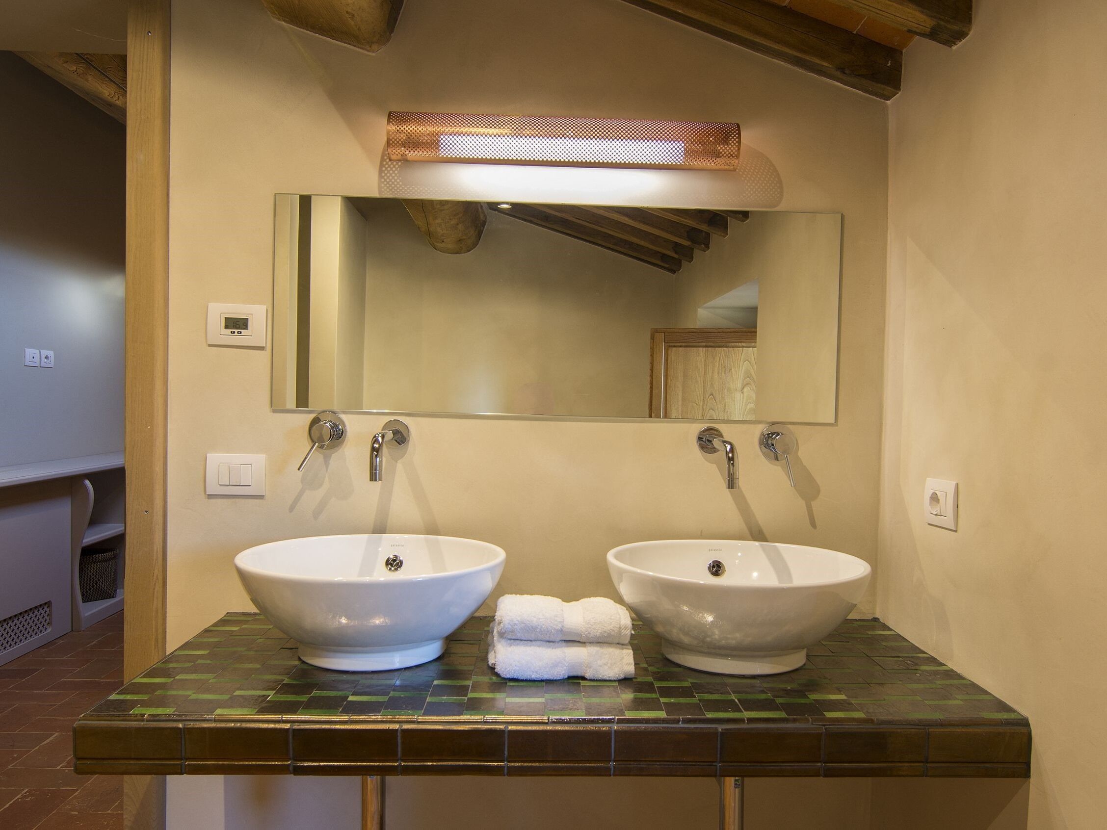 Un baño con dos lavamanos blancos, un espejo y una lámpara sobre el espejo.