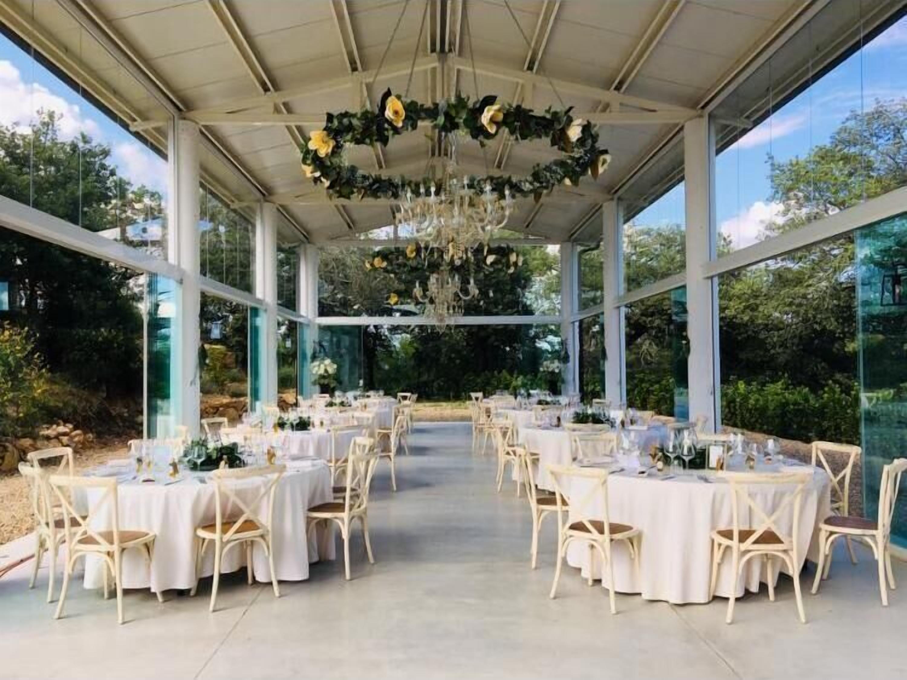 An indoor venue with round tables and chairs, large windows, and a ceiling adorned with floral decorations.