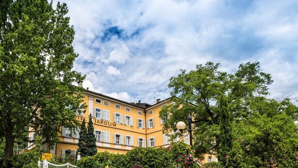 Un edificio amarillo con el letrero "HOTEL KAROLIM", rodeado de vegetación exuberante y plantas con flores.