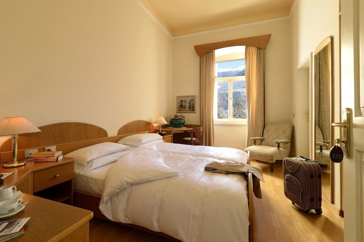 A hotel room with a bed, bedside table, lamp, chair, and a suitcase.