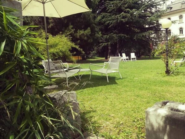 A grassy outdoor area with several white metal chairs and a large umbrella.