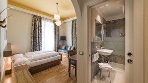 Habitación de hotel con cama, escritorio, silla, televisor y baño con ducha y lavamanos.