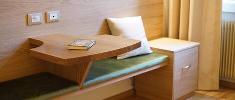 A compact room with a built-in bench, a small bedside table, and a drawer unit.