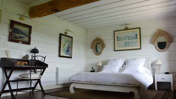 A bedroom with a bed, a desk, and a chair. There are paintings on the walls and a mirror above the bed.