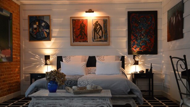 Un dormitorio con una cama grande, dos mesitas de noche, un jarrón decorativo y obras de arte en las paredes.