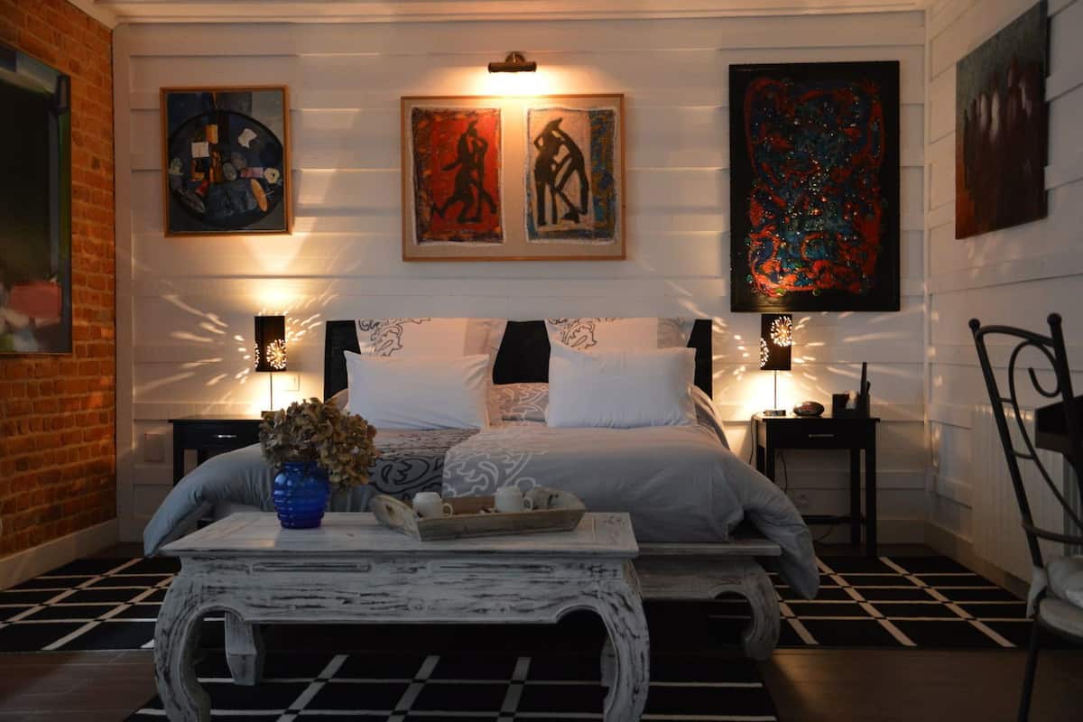A bedroom with a large bed, two bedside tables, a decorative vase, and artwork on the walls.