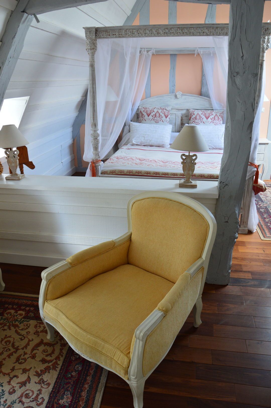 A bedroom with a four-poster bed, a yellow armchair, and a wooden floor.