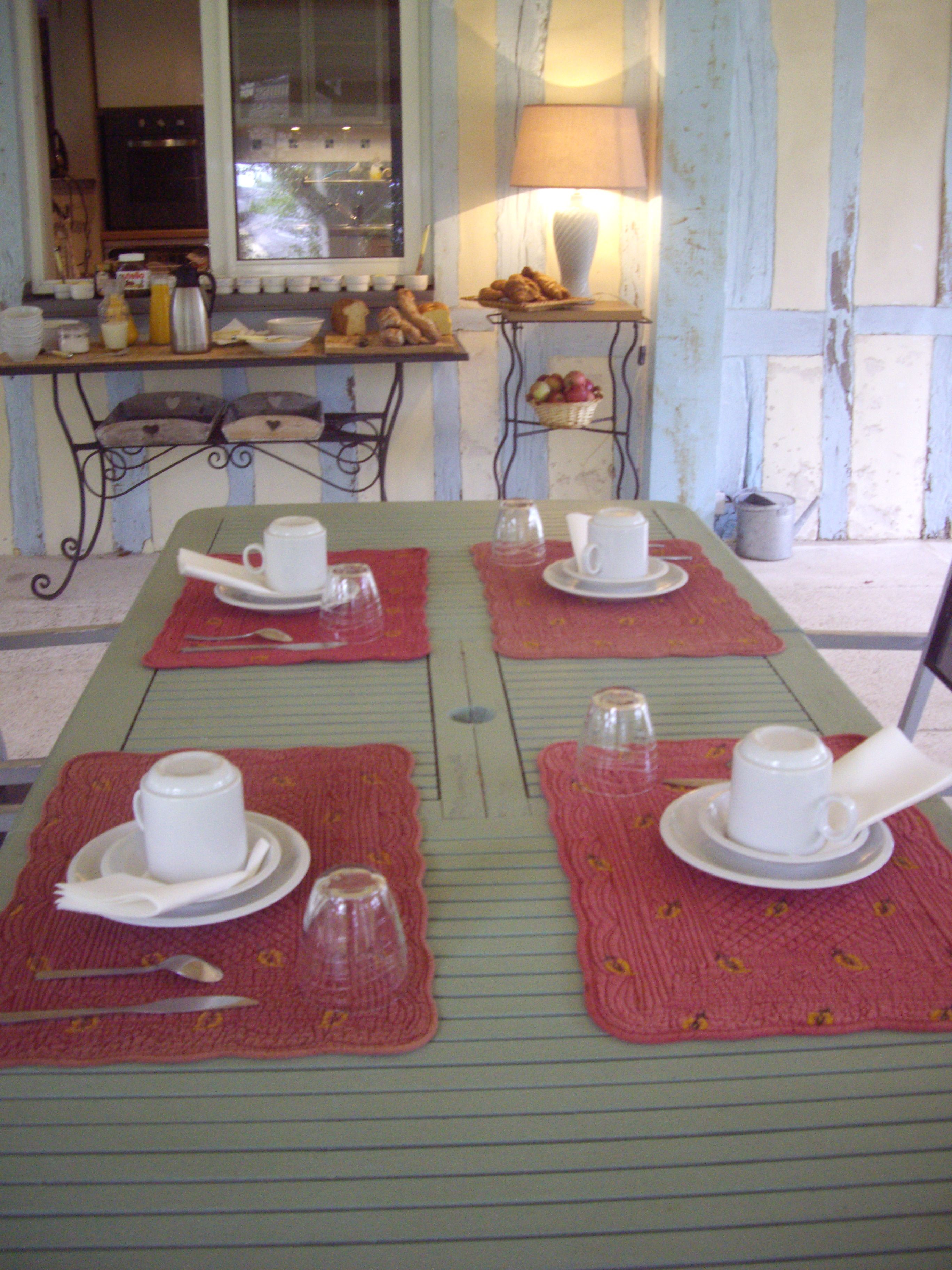 A dining table set with white cups and saucers, red placemats, and a window with a view of the street.