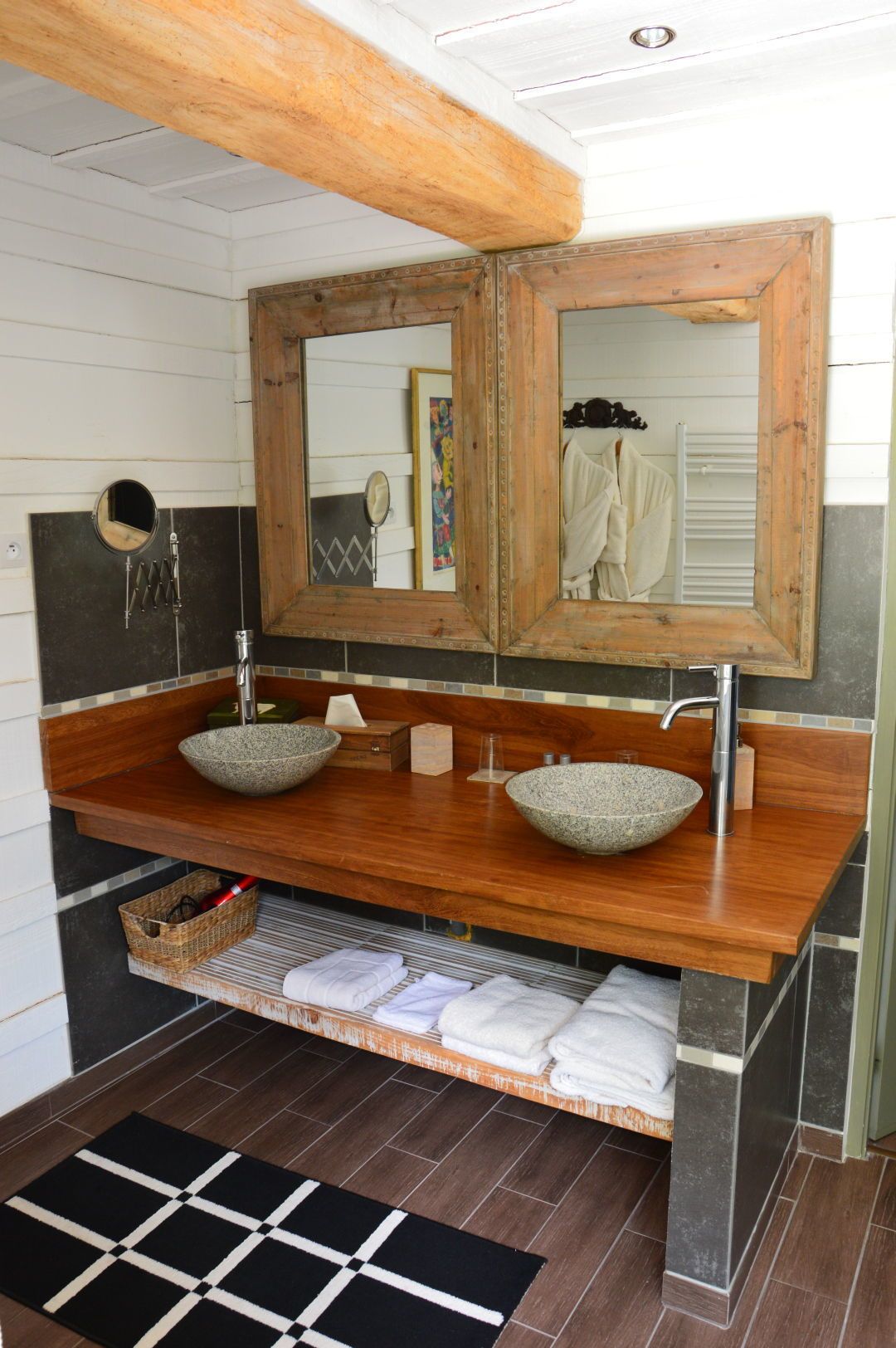 A bathroom with two vessel sinks, a wooden vanity, a large mirror, and a black and white checkered rug.
